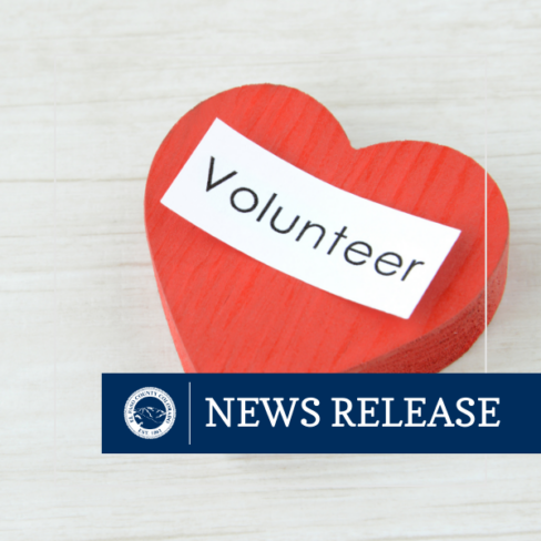 square graphic image of a wooden red heart with a white strip of paper with the word Volunteer laying on top of the heart with blue rectangle with text NEWS RELEASE