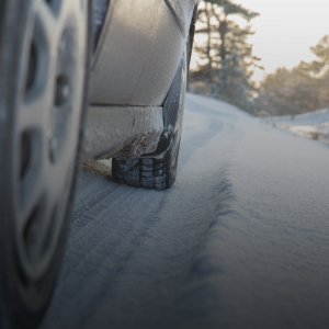 The bottom half of a car showing its wheels driving on a snowy road