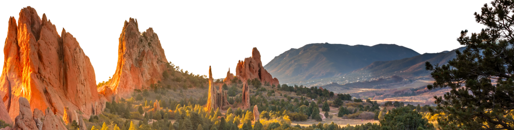 Image of Garden of the Gods at sunrise in Colorado Springs. Tall red rocks are highlighted by the golden sun with Cheyenne Mountain in the background.