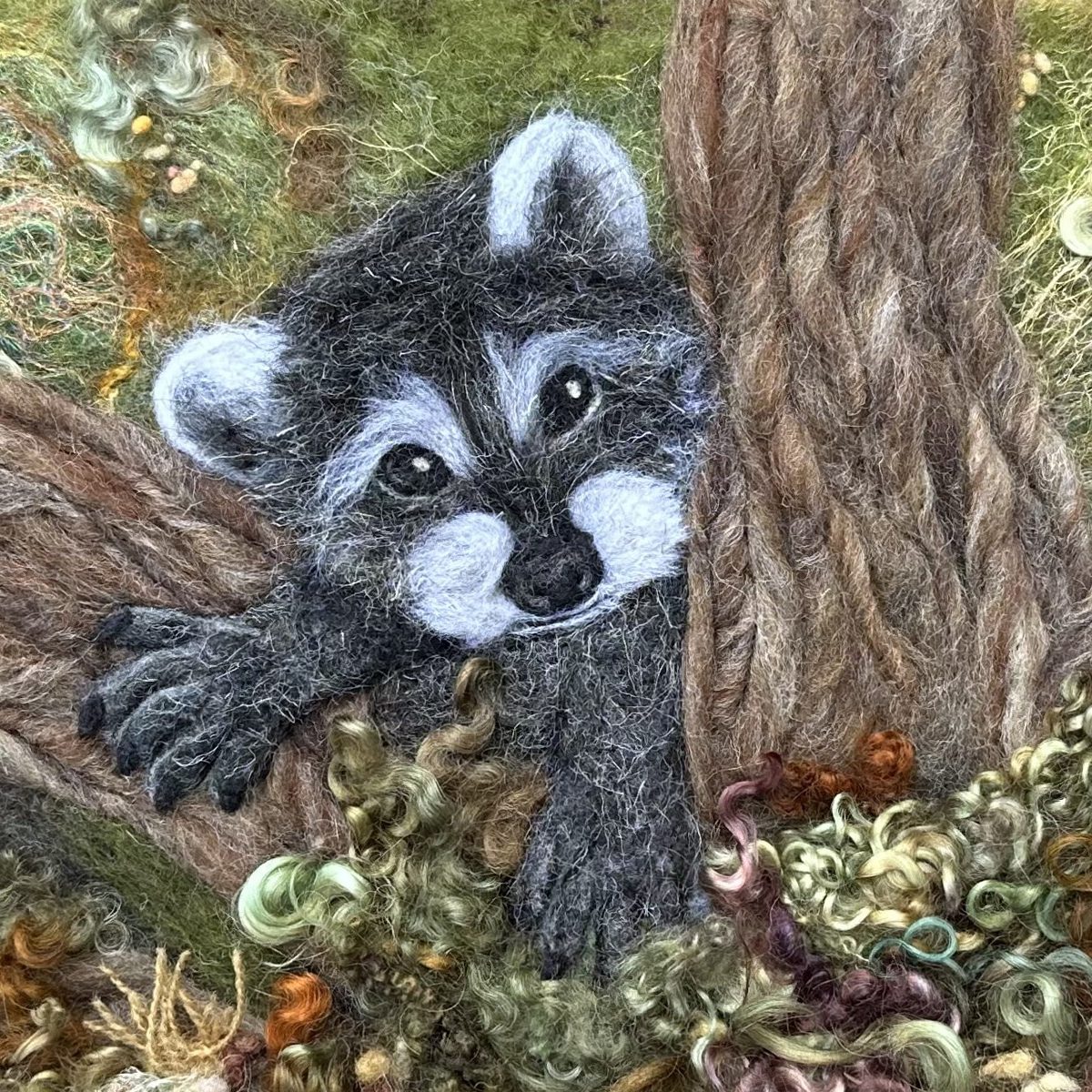 Fiber art of a raccoon sticking out between two tree branches.