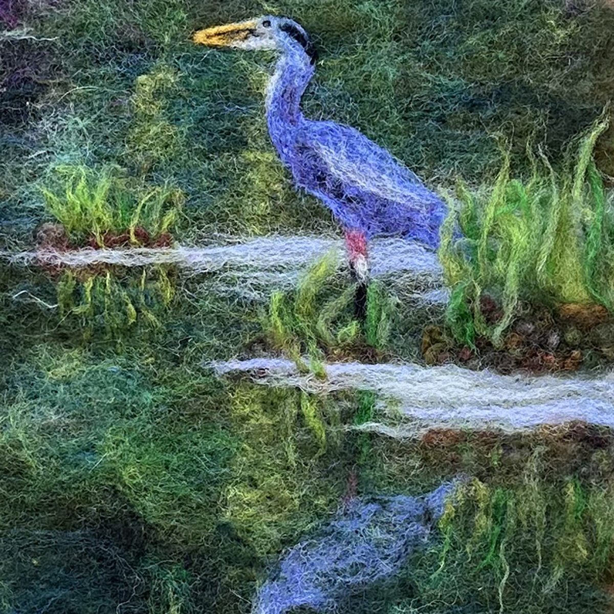 Fiber art of a great blue heron and it's reflection at the edge of a pond