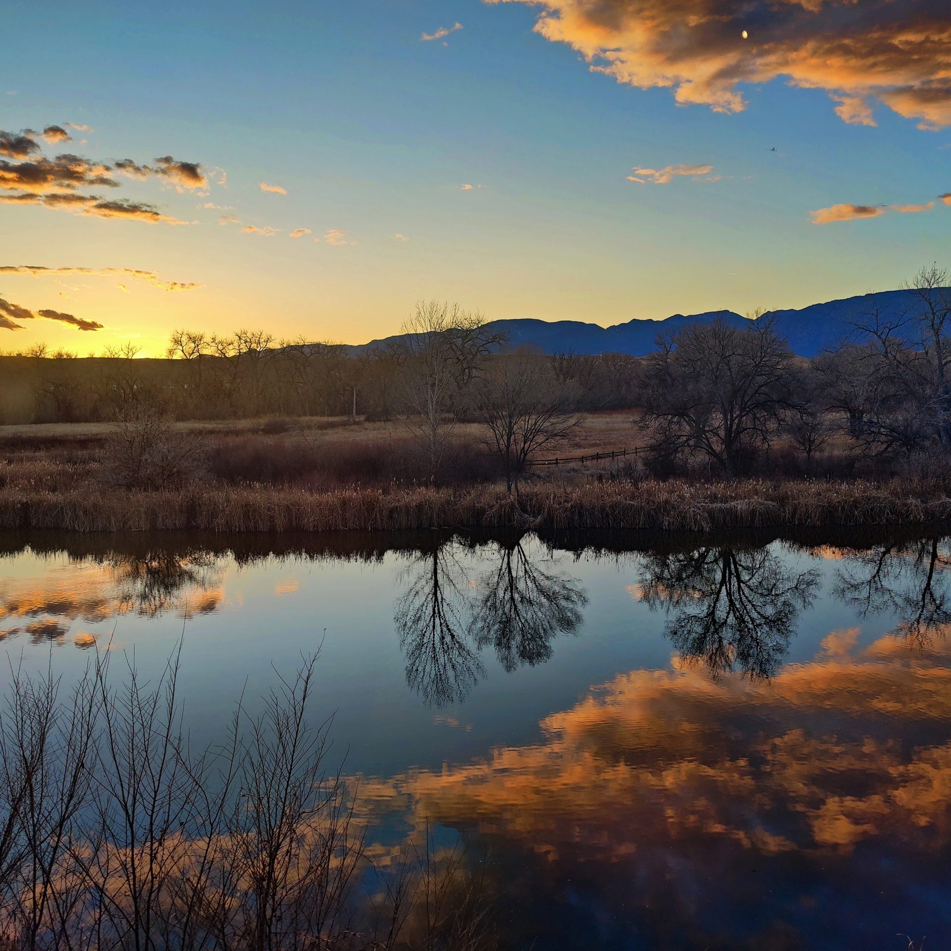Photo of a sunset behind a mountain with a pond in the foreground
