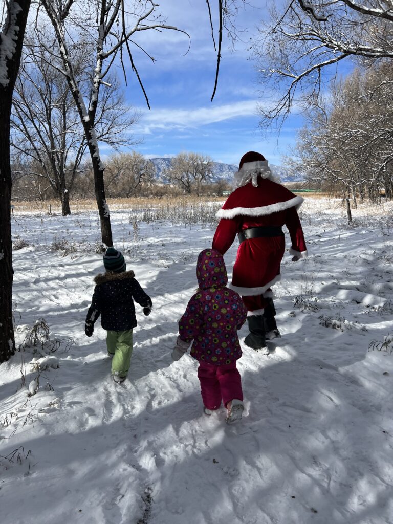 Santa strolls along a snowy trail with two children.
