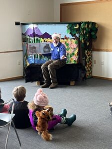 A man wearing a Santa hat reads to a room of children.