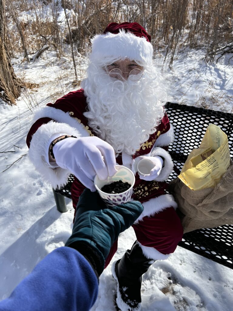 Santa passes a cup of birdseed to a gloved hand.