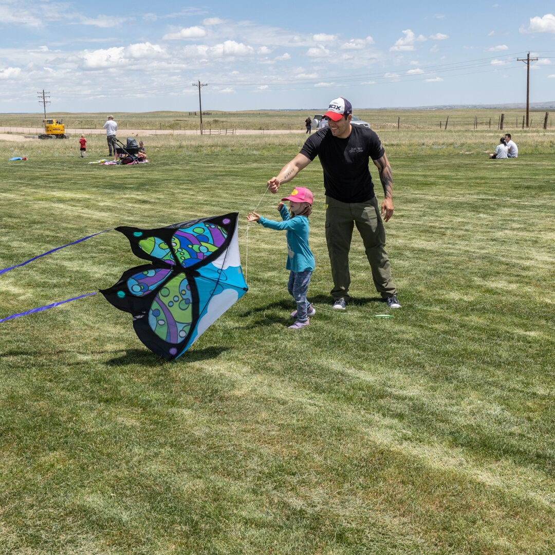 Adult helpd small child hold butterfly shaped kite in an open grassy area