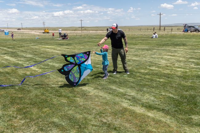 Adult helpd small child hold butterfly shaped kite in an open grassy area