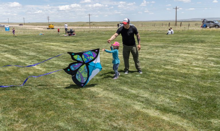 Adult helpd small child hold butterfly shaped kite in an open grassy area