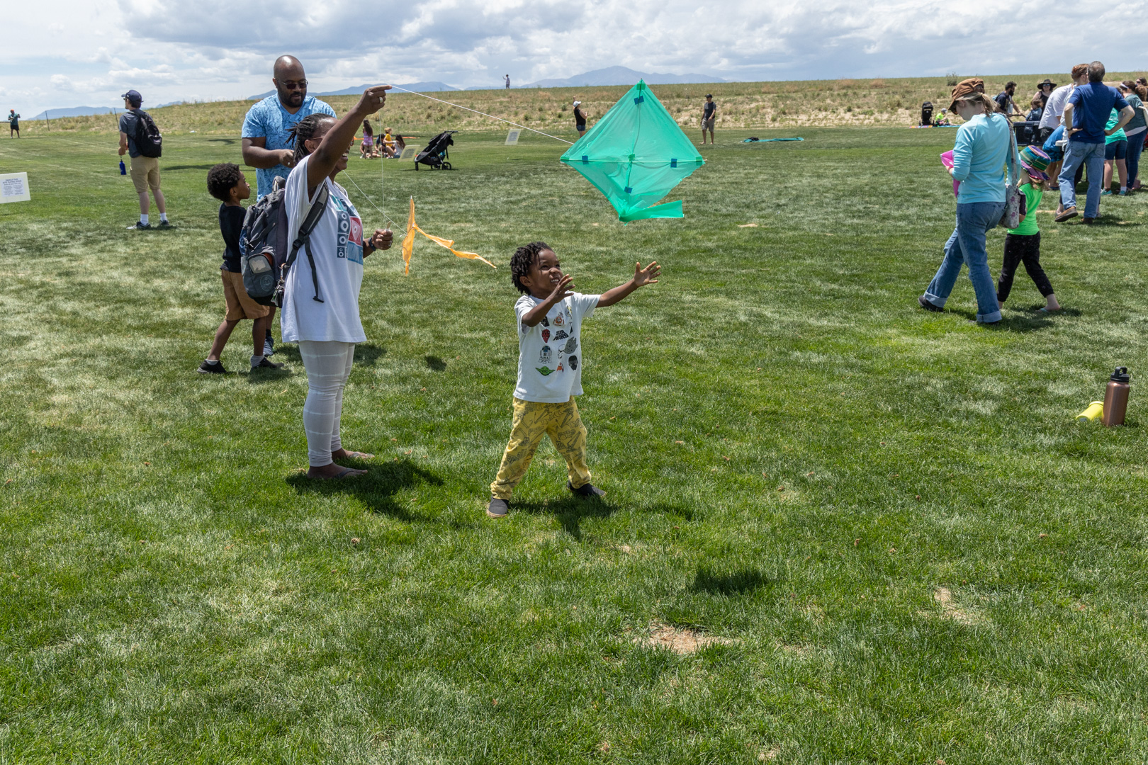 Young child holds kite above head while other people walk in background