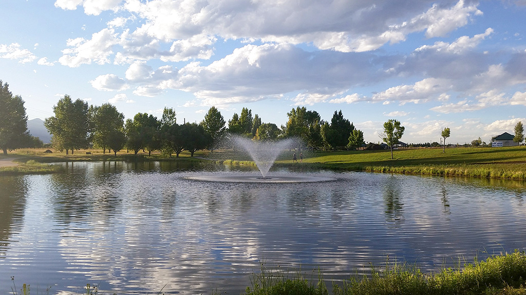 Fountain in pond a fountain is spraying water upward in a v-formation over a pond which is reflecting a puffy clouds with a blue sky