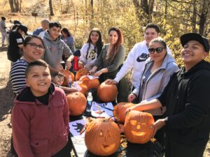 A family smiles as they carve pumpkins into jack-o-lanterns outside on a fall day.